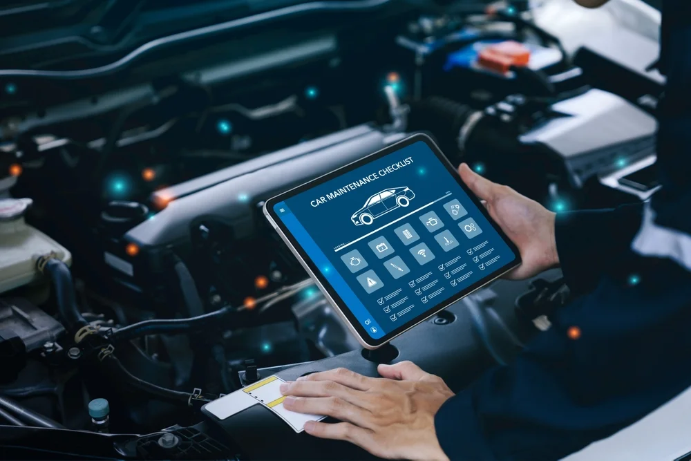 Technician holding a vehicle checklist tablet over an open engine bay