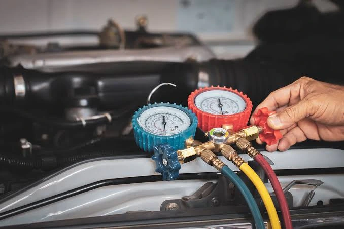 Technician holding manifold gauges beside a vehicle engine bay