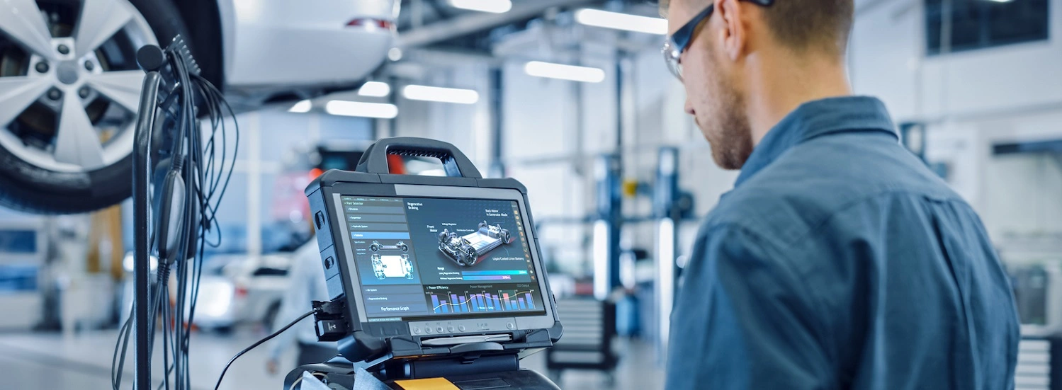 Technician using diagnostic equipment beside a raised vehicle in a workshop